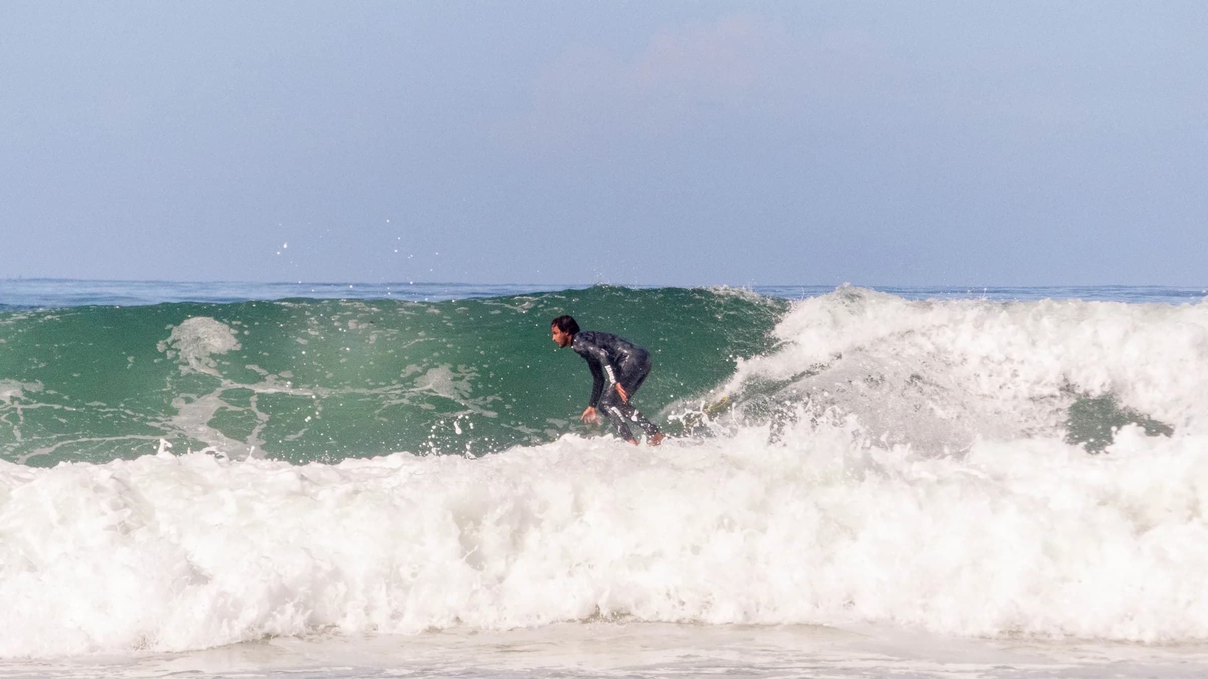 Guests in Sunset Surf House wetsuits laughing together behind a green foam surfboard on the beach