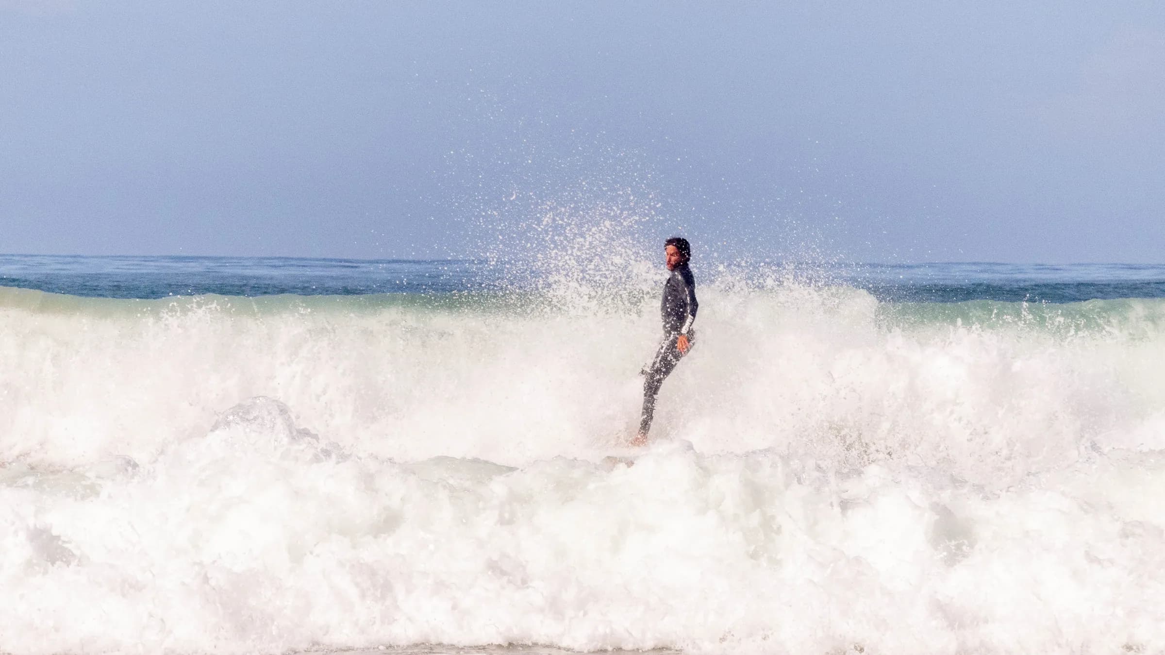 A surf coach kneeling on a board to demonstrate the pop-up while students watch from the sand