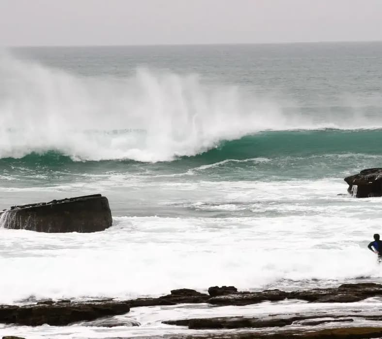 A surfer paddling out past the rocks at Boilers