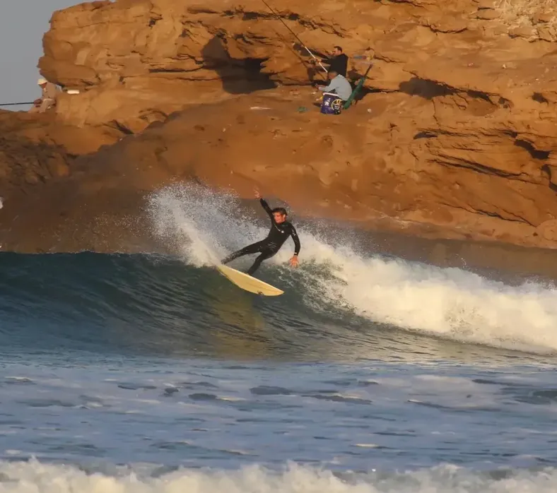A surfer riding along the red cliffs at Devil's Rock