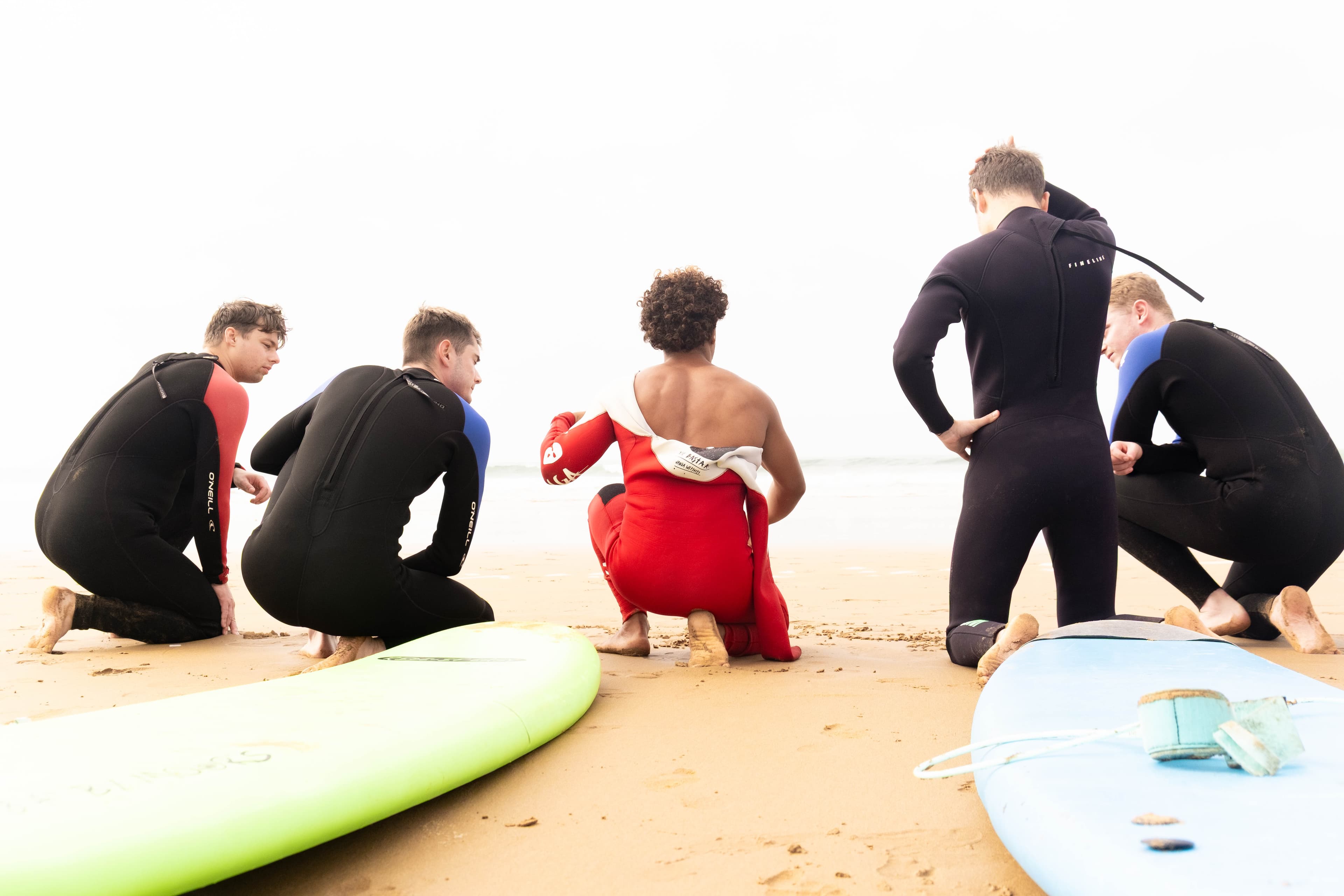 A coach demonstrating a pop-up on the sand while surf students in wetsuits watch from the beach