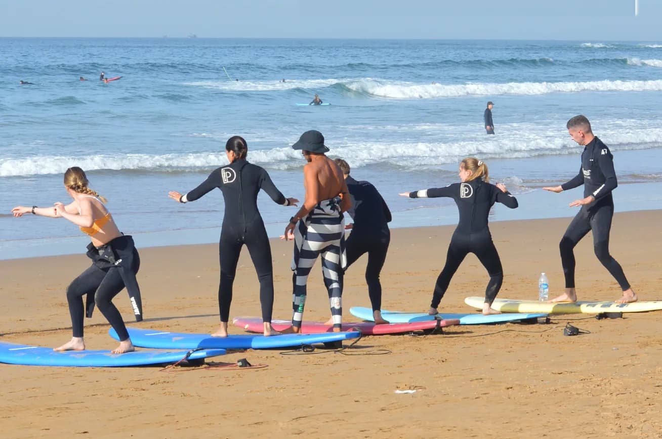 Surf students in a beach warm-up circle under a clear blue sky